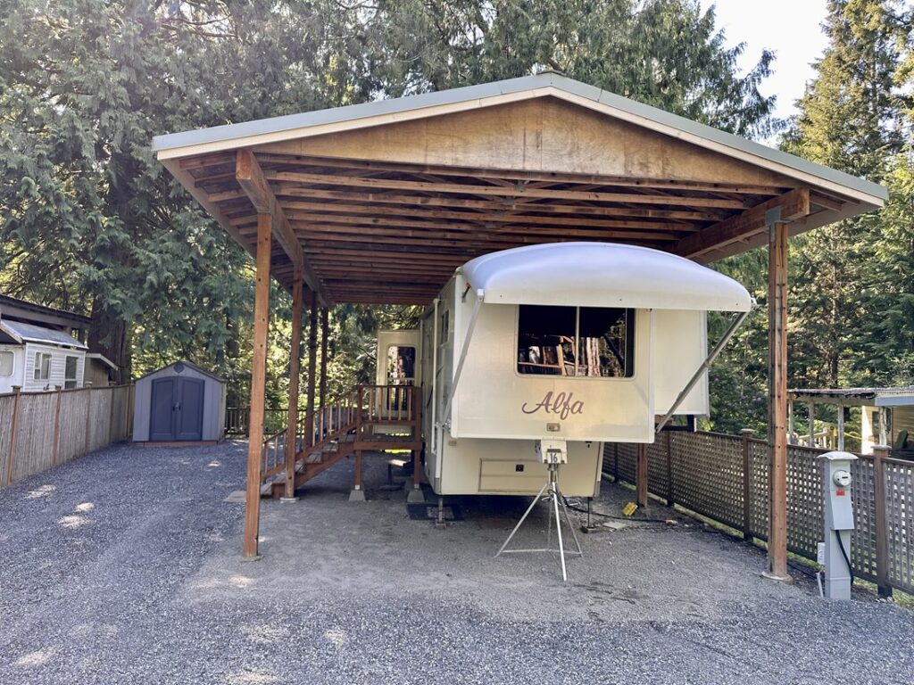 RV under wooden shelter in forested area.